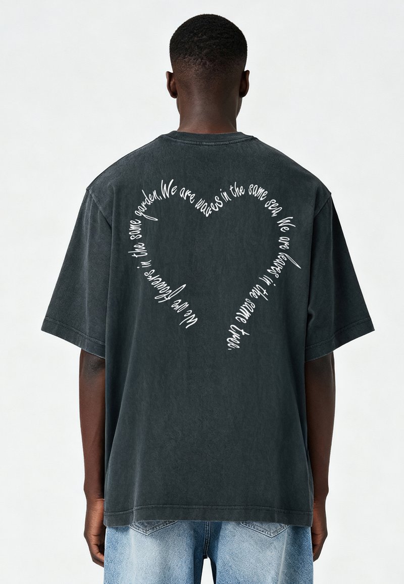 Tumšpelēka, pārāk liela kokvilnas t-kreklu ar izliektiem baltajiem tekstiem sirds formā uz muguras, īsām piedurknēm un brīvu piegriezumu.