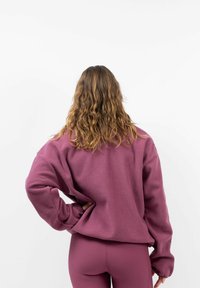 Overmaat, gestructureerde, bordeauxrode sweatshirt met verlaagde schouders en lange mouwen, gecombineerd met bijpassende aansluitende bordeauxrode leggings.