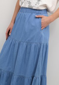 Denim-maksihame, jossa on kerroksellinen muotoilu, vaaleansininen väri, joustava vyötärö ja sivutasku. Sujuva pinta, jossa on rypytystaiheita.