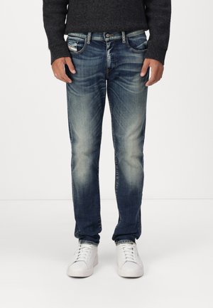 Denim jeans med en falmet mid-blue vask, rette ben, fem-lomme design og subtile slidmærker; parret med hvide sneakers.