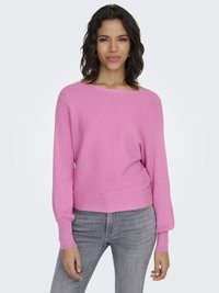 Rosa ribbestrikket genser med bred båthals og lange, lett puffete ermer. Brukt med lysegrå jeans, på en nøytral bakgrunn.