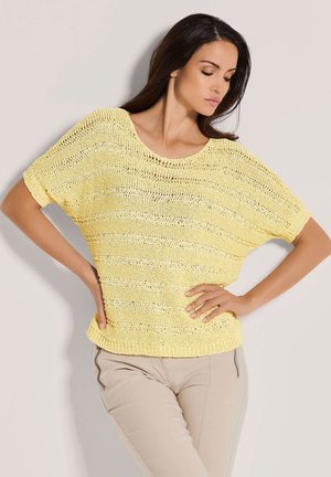 Gelber gestrickter Pullover mit lockerer Passform und weiten Ärmeln, der ein gestreiftes Muster und einen gerippten Saum aufweist. Kombiniert mit hellbeigen Hosen.