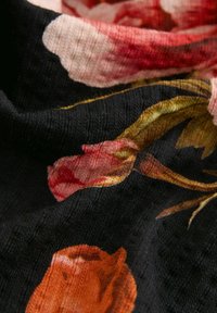 Tissu noir avec une texture douce et côtelée présentant un motif floral dans des tons de rose, orange et vert avec des plis et des rides visibles.