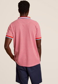 Rood-wit geruit polo shirt met contrasterende rode en blauwe kraag en mouwaccenten, gemaakt van een soepele stof, gecombineerd met marineblauwe shorts.