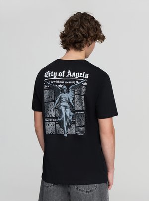 T-shirt nera in cotone con una grande grafica di un angelo grigio con testo in stile giornale sul retro. Girocollo e maniche corte.