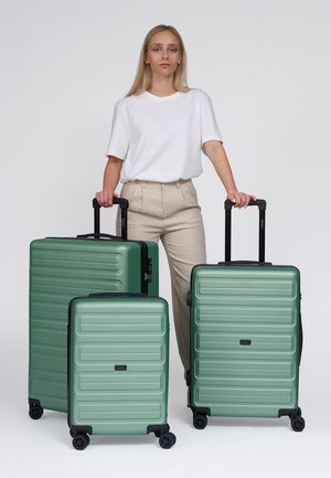 Trois valises rigides vertes avec un design embossé linéaire, finition mate et poignées rétractables, positionnées côte à côte.