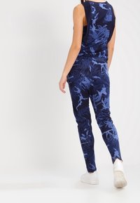 Top in blu navy senza maniche e pantaloni abbinati con una fantasia di foglie in diverse tonalità di blu; tessuto morbido, vestibilità slim, abbinati a scarpe bianche.