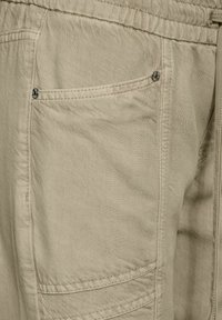 Pantalones cargo beige con tejido texturizado, que cuentan con un bolsillo trasero con un botón de presión metálico y costuras en contraste a lo largo de las costuras.
