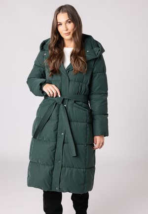 Manteau long matelassé en vert foncé, avec une taille ceinturée, une grande capuche et des coutures visibles. Texture douce et brillante avec des fermetures à pression.