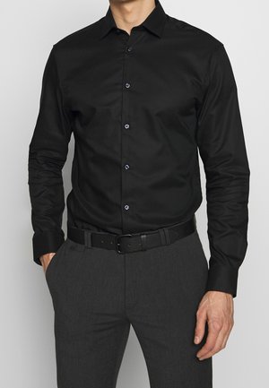 Chemise habillée noire à manches longues avec un col pointu, dotée de boutons bleus et d'un léger éclat, associée à un pantalon gris et une ceinture noire.