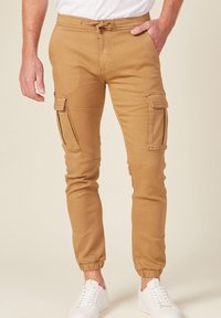 Khakifärgad joggerbyxor med elastiska muddar, två sidofickor, midjeband med dragsko och blandning av bomull, i kombination med vita sneakers.