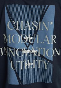 Tamno plavi materijal s geometrijskim uzorcima i velikim tekstom u zlatnoj i svijetloplavoj boji. Ističe riječi poput "Chasin'" i "Modular Technology".