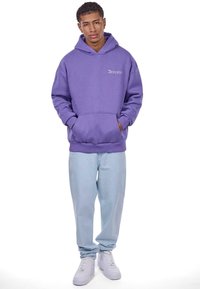 Lilla hoodie med kengurulomme, ribbede manchetter og kant. Sammen med lyseblå løstsiddende jeans og hvide sneakers. Logo på brystet.