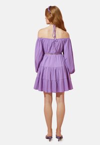 Lila schulterfreie Kleid mit langen Ärmeln, gestuftem Rock, strukturiertem Stoff und tailliertem Schnitt. Styliert mit passendem Haarschmuck.