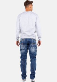 Felpa grigia e jeans in denim blu con più tasche con zip e dettagli sbiaditi. Vestibilità casual, tessuto strutturato e dettagli cuciti.
