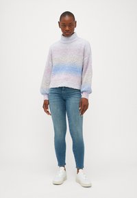 Lahka, pulover v pastelnih barvah s turtleneck ovratnikom in puhasto teksturo, v kombinaciji z modrimi skinny jeans hlačami in belimi supergami. Skrajšana zasnova, balonski rokavi.