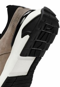 Sneaker en cuir texturé marron vue de profil, avec une semelle en caoutchouc noire et blanche, présentant un motif de crampons pour traction et soutien.