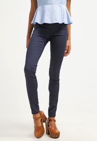 Marina smala jeans med en slät textur. Matchas med bruna plattformshälar. Toppens färg är ljusblå och har en peplum-design.