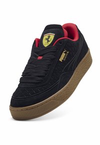 Crne suede tenisice s crvenim detaljima, gumeni potplat, kviltana tekstura, zlatno brendiranje i logo štita na jeziku.