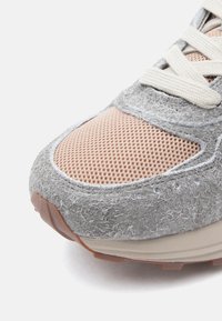 Szare i beżowe sneakersy z teksturowanym, filcowym wykończeniem, z siateczkowymi panelami, wyraźnym sznurowaniem i gumową podeszwą.