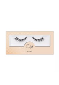 Czarne sztuczne rzęsy w przezroczystej plastikowej tacki, o różnych długościach i grubościach, na beżowym tle z kropkowanym wzorem.