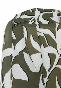 Patterned fabric features large white leaves on an olive green background. The texture is smooth with a slight sheen; a tailored waistband is visible.