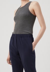 Débardeur gris en tissu côtelé, associé à un pantalon bleu marine à taille élastique avec poches latérales et une texture lisse.