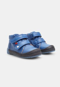 Scarpe in pelle blu con due cinturini in Velcro, suole in gomma, design a bassa apertura e accenti neri a contrasto sulla suola e sulle cuciture.