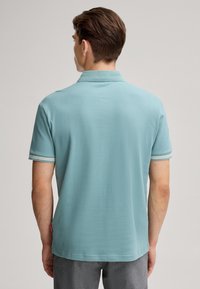 Polo bleu clair en tissu texturé, doté d'un col, de manches courtes et d'accents rayés sur les poignets.