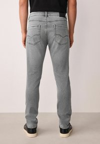 Szürke farmernadrág vékony szabással, két kimért rombusz alakú varrással díszített hátsó zsebbel, fekete tornacipővel párosítva.