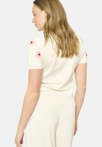 Cream short-sleeve sweater with floral embroidery in pink and red on shoulders; fitted design and ribbed hem and cuffs. Smooth texture.