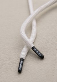 Gros plan sur des lacets tressés blancs avec des embouts noirs étiquetés "DIMBRE" sur un fond de tissu beige.