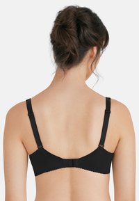 Reggiseno nero con spalline regolabili, bordi ondulati e chiusura con gancio e asola sul retro. Realizzato in tessuto morbido ed elasticizzato per un maggiore comfort.