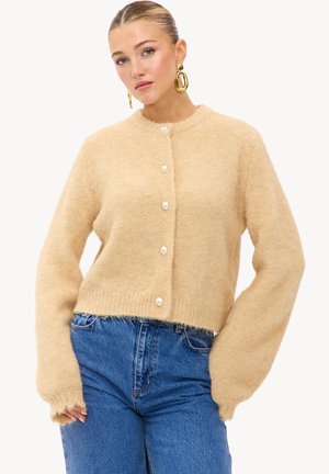 Cardigan en tricot beige avec un col rond, fermetures à boutons en perles et manches allongées. Tissu texturé et doux, avec une longueur cropped.