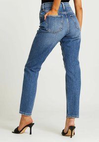 Höga blå jeans med rak passform, med bakfickor och fransade kanter vid fållen. Bärs med svarta klacktofflor.