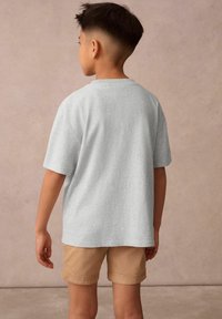 Grå bomullströja med korta ärmar, rundad halsringning och en avslappnad passform, i kombination med beige shorts. Bakgrund i en mjuk neutral ton.
