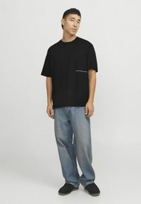 Sort bomulds T-shirt med afslappet pasform, korte ærmer, der har en hvid trykt detalje på venstre side, sat sammen med blå jeans.