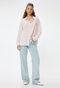 Lys pink skjorte med knapper lavet af let materiale, parret med løse, lyseblå jeans og hvide spidse sko.