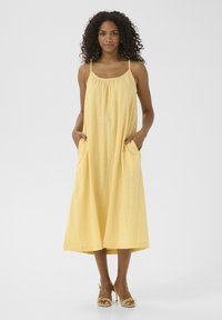 Gelbes Leinen-Midikleid mit verstellbaren Spaghetti-Trägern, gerafftem Ausschnitt und seitlichen Taschen. Glatte Textur mit lockerer Passform.