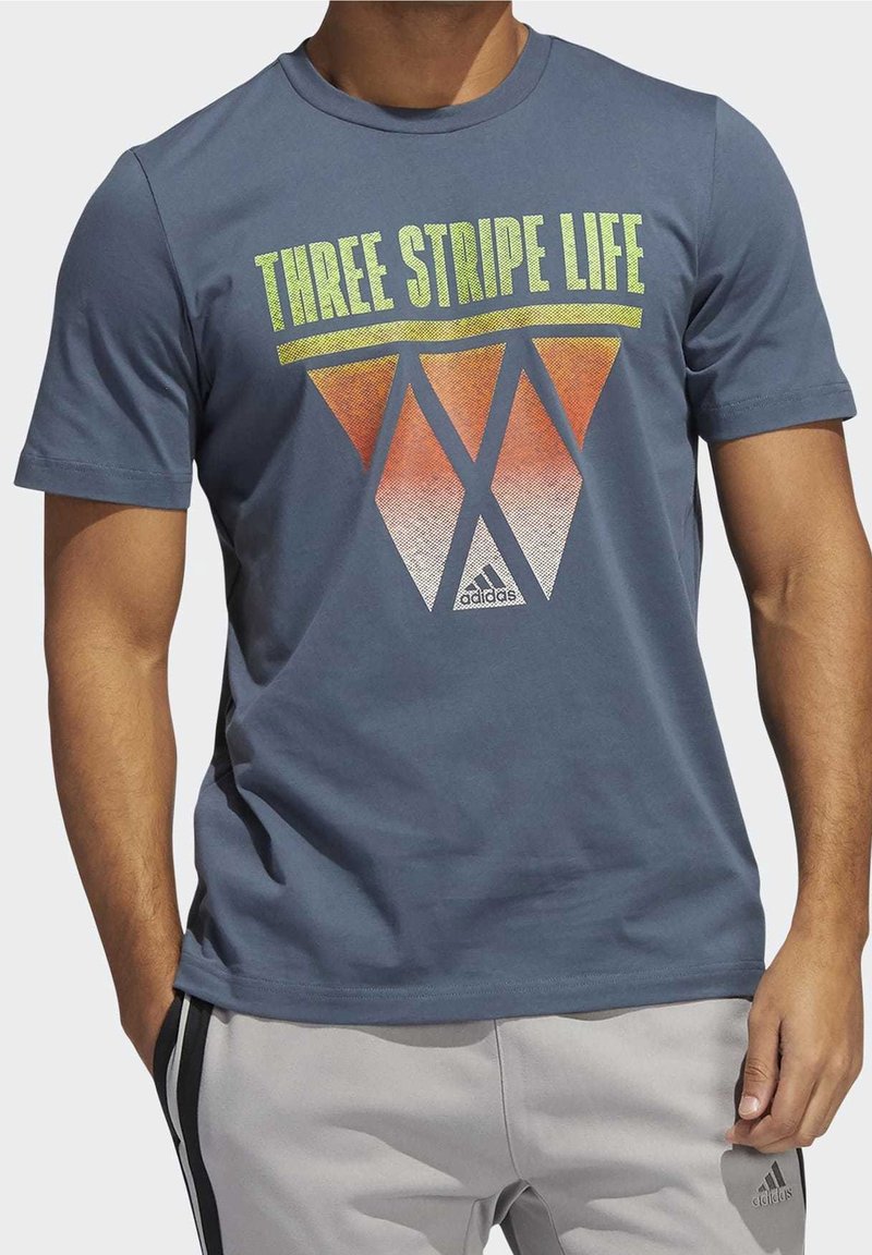 Modrá bavlněná tričko s grafikou "Three Stripe Life" v žlutých a oranžových trojúhelníkových tvarech, s logem Adidas dole.