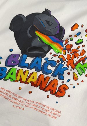 Wit T-shirt met een grote zwarte gorilla-afbeelding waar regenboogkleurige strepen uit de mond komen, omringd door kleurrijke tekst en fragmenten.