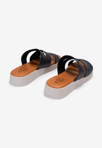 Chanclas negras con dos tiras anchas, plantillas acolchadas marrones y suelas de plataforma texturizadas blancas con diseño estriado.