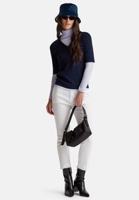 Námořnický V-čelní top vrstvený přes světle fialový rolák, bílé kalhoty, černou kabelku a černé kožené boty na podpatku. Klobouk typu bucket a sluneční brýle.