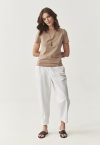 Beige kortærmet top, hvide tapered bukser, brune klipklapper; glat tekstur, enkelt design, minimalistisk stil uden mønstre eller accenter.