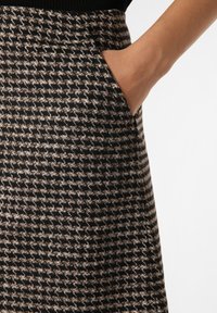 Jupe longueur genoux arborant un motif pied-de-poule en tissu noir et beige. Détail de poche latérale visible sur le côté gauche.