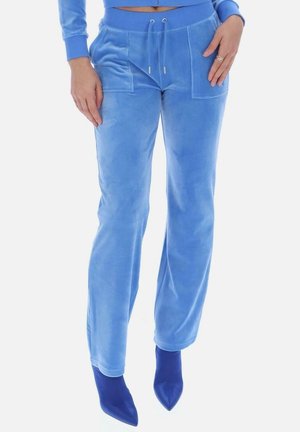 Donna che indossa pantaloni in velluto azzurro chiaro con tasche frontali e coulisse, abbinati a stivali blu scuro con punta a mandorla, mani appoggiate sui fianchi.