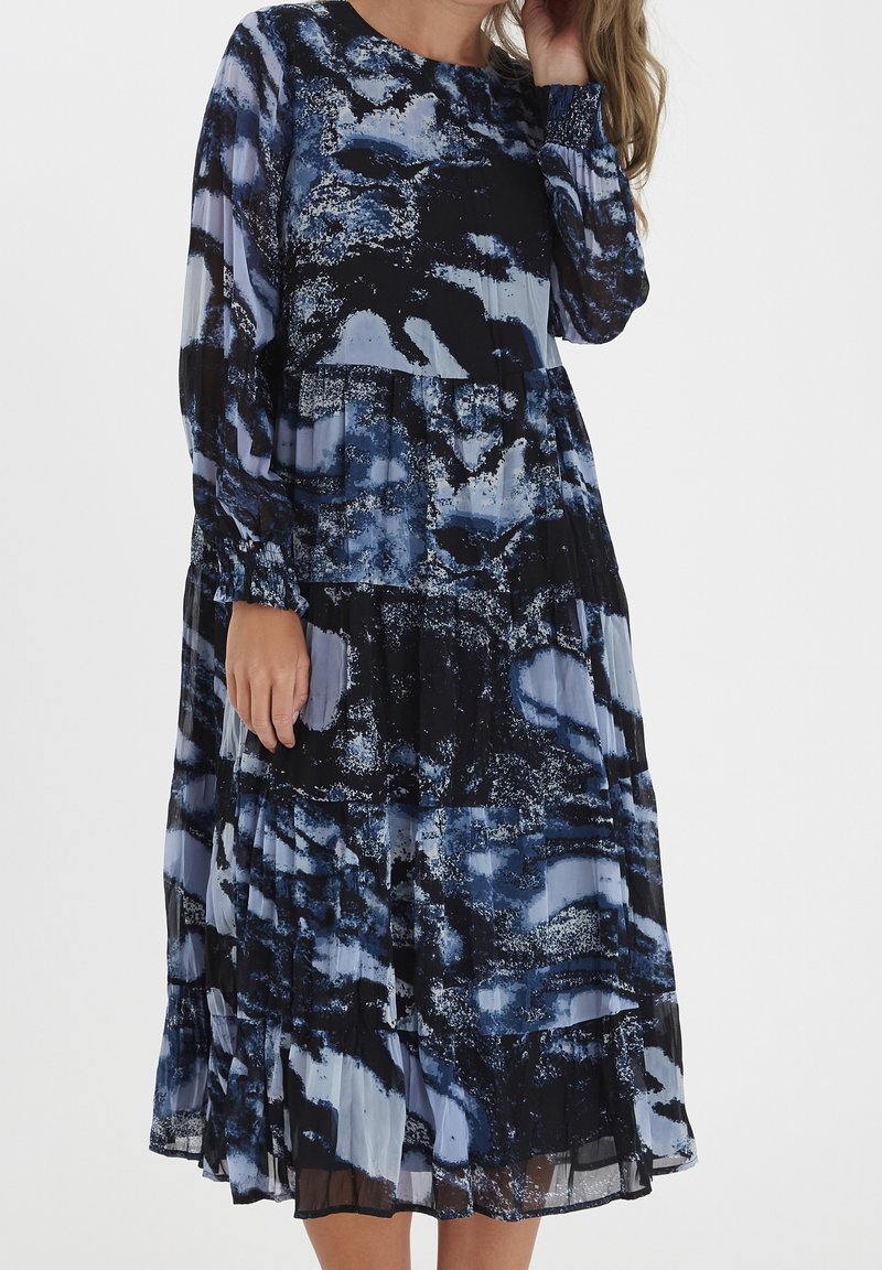 Vestido maxi con un patrón abstracto en azul y negro, que presenta mangas largas, escote redondo y pliegues en capas. Fabricado con tela ligera.