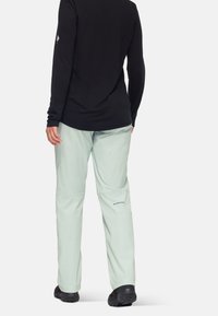 Lichtgroene hikingbroek van synthetisch materiaal, met een elastische tailleband en een logo op het onderbeen. Gepaarde met een zwart langmouwtop.