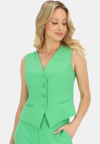 Zielony bezrękawnik o dopasowanym kroju, z dekoltem w serek, pięcioma guzikami i kieszeniami bocznymi. Wykonany z gładkiego materiału o usztywnionym wyglądzie.