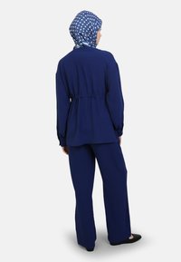 Navyblauwe twee-delige outfit met een lange mouw top met een tailleband en wijde broekspijpen, aangevuld met een gestreepte blauwe sjaal.